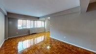 Located at 510 21st St NW in Washington, DC, this single-floor residence offers a well-organized layout that balances open living space with functional private areas. The living room is a standout feature, showcasing beautifully polished parquet wood flooring in a rich herringbone-style pattern that reflects natural light throughout the room. A generous bank of windows along one wall floods the space with natural light and provides views of the surrounding neighborhood, creating an airy and inviting atmosphere. Neutral gray walls complement the warm tones of the flooring, giving the space a clean, contemporary feel. Built-in shelving adds practical storage within the living area. The kitchen is thoughtfully updated, featuring crisp white shaker-style cabinetry, light granite countertops, subway tile backsplash, and stainless steel appliances including a gas range and over-the-range microwave — a setup well-suited for everyday cooking. The bathroom maintains a classic aesthetic with white subway tile wainscoting accented by a black tile border, a wall-mounted mirror, and clean, simple fixtures. A dedicated hallway connects the living and private areas, with additional closet space providing ample storage. This residence combines timeless design elements with modern updates in a prime Northwest Washington location.