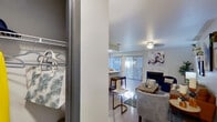 This well-designed single-floor residence offers a thoughtfully arranged layout that balances comfort and modern style throughout. The living room serves as the heart of the home, anchored by a striking marble-surround fireplace and accented with curated wall art, decorative shelving, and an eclectic mix of seating that creates an inviting, personality-rich atmosphere. Large sliding glass doors allow generous natural light to pour in, while vertical blinds provide privacy and light control. The adjacent dining area features additional window coverage, including horizontal blinds and sheer curtains, framing a pleasant outdoor view. The kitchen is outfitted with gray shaker-style cabinetry, light stone countertops, a white subway tile backsplash, and a full suite of stainless steel appliances, offering both functionality and contemporary appeal. The bedroom is a calm retreat, finished with soft carpet, a ceiling fan, and window treatments that allow for restful light levels. A dedicated closet with a rod and shelving system provides organized storage. The bathroom is finished with gray cabinetry matching the kitchen, marble-style countertops, a well-lit vanity mirror, and a tub-shower combination with marble-patterned tile surround. Light wood-style flooring runs throughout the main living areas, unifying the space with a clean, modern aesthetic.