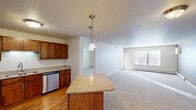 This single-floor residence offers a thoughtfully designed layout that balances functionality and comfort. The open-concept kitchen and living area serves as the heart of the home, where rich warm-toned wood cabinetry pairs with granite-style countertops and a full suite of stainless steel appliances, including a refrigerator, range, microwave, and dishwasher. A central island with pendant lighting above provides additional workspace and casual dining space, while hardwood-style flooring anchors the kitchen. The adjoining living area is carpeted and filled with natural light from large windows, with a door leading to an exterior access point. Two generously sized bedrooms feature plush carpeting and ample closet space, including a walk-in closet in one room. The primary bathroom is equipped with a wide vanity, warm wood cabinetry, a large mirror, tile flooring, and accessibility grab bars. A second full bathroom offers a tub-shower combination and matching tile flooring. A dedicated laundry closet houses a stacked washer and dryer unit alongside wire shelving for additional storage. Neutral tones and textured ceilings are consistent throughout, creating a clean and move-in-ready environment.