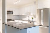 Located at 1249 N Shore Blvd E in Burlington, Ontario, this two-bedroom, one-bathroom unit offers a well-organized layout across a single floor. The open-concept living and dining area is finished with distinctive parquet flooring throughout and features large windows fitted with baseboard heating units, allowing natural light to fill the space while providing views of the surrounding cityscape.

The kitchen is a functional highlight, outfitted with white shaker-style cabinetry, a subway tile backsplash, stainless steel appliances including a French door refrigerator and range, and a dark-topped peninsula that separates the kitchen from the main living area. White floor tiles and recessed lighting complete the clean, contemporary aesthetic.

The primary bedroom is generously sized, benefiting from large windows and parquet flooring consistent with the rest of the unit. A second bedroom offers similar finishes and natural light. Both bedrooms are serviced by a well-appointed four-piece bathroom featuring white subway tile surround, a soaking tub with shower, grey floor tiles, and a vanity with mirror. A hallway connects the rooms, which also includes a closet with mirrored sliding doors, adding a sense of depth to the space.