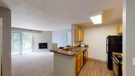 This single-floor residential unit offers a well-designed, functional layout that balances open communal spaces with comfortable private areas. The heart of the home is an open-concept kitchen and living area, where the kitchen features warm honey-toned cabinetry, granite-style countertops, wood-look flooring, a peninsula with a sink, and black appliances including a refrigerator, electric range, built-in microwave, and dishwasher. A skylight above the kitchen adds a bright, airy quality to the space. The living area flows seamlessly from the kitchen and is anchored by a fireplace, with sliding glass doors that invite natural light and provide access to an outdoor area. The bedrooms are carpeted and generously sized, each equipped with ceiling fans and windows that bring in natural light. The primary bathroom is a standout feature, offering a dual-sink vanity with granite-style countertops, warm wood cabinetry, wood-look flooring, and a large mirror with modern lighting. The floor plan also reveals a dedicated in-unit laundry area, adding everyday convenience. Neutral gray walls and consistent finishes throughout lend the space a cohesive, move-in-ready aesthetic.