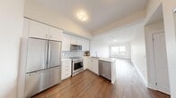 This single-floor unit offers a well-designed layout across three bedrooms and two bathrooms. The open-concept kitchen flows seamlessly into the living area, creating a cohesive and functional living space. The kitchen is outfitted with a full suite of stainless steel appliances, including a refrigerator, range, built-in microwave, and dishwasher. White cabinetry extending to the ceiling maximizes storage, while a mosaic tile backsplash and light stone countertops add a clean, contemporary aesthetic. A peninsula with a double sink completes the kitchen.

The living area features elevated ceilings and a large window framing an outdoor view of greenery and a distant cityscape, filling the space with natural light. Hardwood-style flooring runs consistently throughout the living areas and bedrooms, contributing to a cohesive, modern feel. Access to a glazed balcony corridor is available directly from the living room.

The primary bedroom is a generously sized room with direct access to a private bathroom. The additional bedrooms are bright with neutral walls and the same hardwood-style flooring. Both bathrooms are finished in white tile and include modern vanities with integrated sinks, large mirrors, and a bathtub with shower combination.