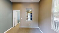 Located at 2415 SE Fourth Ln in Gainesville, Florida, this single-floor space is thoughtfully organized into two distinct rooms: a bedroom and a dedicated exercise room. The exercise room serves as the centerpiece of the space, featuring wall-to-wall carpeting, warm tan-toned walls, and an abundance of natural light streaming through multiple windows fitted with blinds. Skylights and recessed lighting brighten the room further, while a ceiling fan ensures comfortable air circulation. The exercise room is equipped with a variety of fitness machines, including a treadmill, elliptical, stationary bike, and a multi-function cable weight machine, making it a fully functional fitness area. Safety features such as a fire extinguisher are also present. A glass-panel exterior door provides direct access to the outdoors, offering views of surrounding greenery. The bedroom is a well-proportioned room with plush carpeting, cool blue-gray walls, crisp white baseboards, and recessed lighting. It connects to the exercise room through an interior door and includes a pass-through window, adding a practical and open feel to the layout. Together, the two rooms form a functional, light-filled space suited for active living.