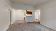 This single-floor, 2-bedroom, 2-bathroom residence offers a practical and comfortable layout across a well-utilized footprint. The living room serves as the heart of the home, featuring a classic wood-framed fireplace, neutral carpet flooring, and a textured ceiling. An arched pass-through opening connects the living area to the kitchen, which is laid out in a galley style with warm wood-toned cabinetry, white appliances including a dishwasher and electric range, a stainless steel double sink, and light-toned laminate countertops. Wood-look flooring runs throughout the kitchen and hallways, providing a clean contrast to the carpeted living and sleeping areas. The primary bedroom offers a comfortable amount of space, a window that brings in natural light, and direct access to the hallway. The second bedroom also features carpet flooring, a window with natural light, and a closet. Both bathrooms are finished with wood-toned vanity cabinetry, speckled countertops, and single-basin sinks with mirrored medicine cabinets above. One bathroom includes a full tub-shower combination with white tile surround and wood-look flooring. The overall aesthetic is clean and functional, with a consistent neutral palette throughout.