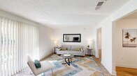 This well-appointed single-story home features 3 bedrooms and 2 bathrooms thoughtfully arranged across a comfortable and efficient floor plan. The living room is a bright, welcoming space with large vertical-blind-covered sliding doors that invite abundant natural light, complemented by wood-look flooring and a textured ceiling. The adjacent dining area flows seamlessly into the kitchen through an open passageway, and features hardwood-style floors and clean white walls. The kitchen is outfitted with white shaker-style cabinetry, open shelving, light tile flooring, a stainless steel dishwasher, range, and refrigerator, along with a window above the sink that keeps the space airy and bright. The bedrooms are calm and restful, each featuring neutral walls, wood-look flooring, ceiling fans with lighting, and windows with blinds offering natural light and privacy. The spacious primary bedroom provides generous room for a comfortable retreat. Both bathrooms maintain a clean, white aesthetic with tub-shower combinations and tiled surrounds. Two closets provide practical storage throughout the home. The overall design is cohesive and light-filled, with a consistently neutral palette that lends the home a fresh, modern feel.