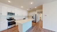 Located at 14951 Foothill Blvd in Fontana, CA, this well-appointed 2-bedroom, 2-bathroom residence offers a thoughtfully designed single-floor layout. The modern kitchen is a standout feature, showcasing crisp white shaker cabinetry extending to the ceiling, a large central island with a clean white countertop, and a full suite of stainless steel appliances including a gas range, built-in microwave, dishwasher, and French door refrigerator. Recessed lighting illuminates the space, complemented by warm wood-look plank flooring that flows throughout the home. The living room is bright and open, featuring a ceiling fan and a sliding glass door that leads to a private balcony with outdoor views, filling the space with natural light. The primary bedroom is generously sized and includes its own dedicated closet. The second bedroom also features wood-look flooring, white walls, and a ceiling fan. Both bathrooms are clean and functional, with one offering a full tub-shower combination. A dedicated laundry area houses a stacked washer and dryer unit, adding everyday convenience. Neutral-toned walls and consistent flooring throughout create a cohesive, move-in-ready aesthetic.