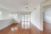 Located at 6106 Yellow Sun Dr in Lake Worth, FL, this two-story home offers 4 bedrooms, 3 bathrooms, and a well-organized layout spread across two floors. The main living level hosts the majority of the home's living space, with rich, polished hardwood flooring running throughout the living room, dining area, kitchen, and bedrooms. The living room is bright and airy, featuring a ceiling fan, multiple windows, and French doors that open to a private patio with views of tropical landscaping — an ideal feature for Florida living. A pendant light and open staircase railing add architectural interest to the space. The kitchen is well-appointed with rich wood cabinetry, granite countertops, stainless steel appliances including a refrigerator, electric range, and microwave, and a breakfast bar that connects to the adjacent dining area. Each of the four bedrooms is finished with hardwood floors, ceiling fans, and ample natural light. The primary bedroom includes its own closet and is served by a full bathroom featuring tile flooring, a glass-enclosed shower with tile surround, and a wood vanity. A dedicated laundry room with full-size washer and dryer adds everyday convenience. The ground level includes an attached garage with a roll-up door. Carpet-lined stairs with a handrail connect the two floors.