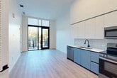 Located at 501 NW Seventh Terrace in Fort Lauderdale, FL, this modern one-bedroom, one-bathroom unit offers a thoughtfully designed open-concept layout with clean contemporary finishes throughout. The combined living, dining, and kitchen area is the heart of the unit, distinguished by soaring ceilings that amplify the sense of space. Light-toned hardwood-style flooring runs throughout, complementing the bright white walls and lending a cohesive, airy feel. Floor-to-ceiling black-framed glass doors open onto a private balcony, flooding the living area with abundant natural light and offering pleasant tree-lined outdoor views. The kitchen features sleek two-tone cabinetry — crisp white upper cabinets paired with matte blue-gray lower cabinets — a white tile backsplash, a matte black faucet, and stainless steel appliances including a dishwasher, range, microwave, and a paneled refrigerator. The bedroom is a well-proportioned retreat accessed through a stylish sliding barn door with matte black hardware, continuing the modern aesthetic. The bathroom is finished with large-format tile flooring, a navy blue vanity with a white countertop, and a full tub and shower. Three closets and an in-unit laundry area provide excellent storage and convenience throughout this efficiently designed Fort Lauderdale residence.