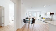 Located at 5711 John F. Kennedy Blvd in West New York, NJ, this thoughtfully designed single-floor residence showcases a clean, modern aesthetic throughout. Light hardwood flooring flows seamlessly across the open-concept living, dining, and kitchen areas, creating a cohesive and airy atmosphere. The living room is generously proportioned, anchored by large floor-to-ceiling windows and a glass door that opens onto a private balcony, flooding the space with natural light and offering views of the surrounding neighborhood. The dining area sits adjacent to the living room, providing an effortless transition between spaces. The kitchen is a standout feature, outfitted with high-gloss white cabinetry, a tile backsplash, stainless steel appliances including a French door refrigerator and gas range, and a large center island with bar seating and pendant lighting overhead. The bedrooms are bright and well-proportioned, each with large windows that invite natural light. The primary bedroom offers a serene, minimalist retreat, while the secondary bedroom provides ample flexibility. The bathroom is finished with large-format marble-look tile, a warm wood floating vanity, gold fixtures, and a mirrored medicine cabinet, delivering a spa-like ambiance.