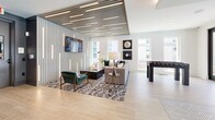 Located at 3314 Piedmont Rd NE in Atlanta's prestigious Buckhead district, this thoughtfully designed amenity lounge offers a dynamic, open-plan layout across a single well-appointed floor. The space is anchored by a striking gold brushstroke mural that adds an artistic focal point near the entrance, where black-framed glass doors open to an outdoor pool area, flooding the interior with natural light.

The lounge is divided into distinct activity zones that flow seamlessly into one another. A game area features a shuffleboard table, billiards table, and foosball table, catering to a variety of recreational interests. Nearby, a stylishly furnished seating area showcases a plush sectional sofa, curated artwork including vinyl record wall pieces, and an elegant slatted feature wall with integrated linear lighting that adds depth and visual interest to the space.

The kitchen bar area is equally impressive, centered around a large island with seating for several guests, illuminated by a trio of gold pendant lights. Bold geometric-patterned tile flooring, dark-framed windows, and clean white walls complete the modern aesthetic. Light wood-look flooring runs throughout, tying all zones together with a cohesive, contemporary feel. Multiple large windows ensure the space remains bright and connected to its urban surroundings.