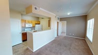 This single-floor residential unit offers a functional and comfortable layout designed for everyday living. The open-concept living and dining area is finished with plush wall-to-wall carpeting and crown molding, with a ceiling fan overhead adding both style and practicality. Large windows and a sliding glass door flood the living space with natural light while providing views of the surrounding exterior. The entryway features tile flooring that transitions seamlessly into the carpeted living area, creating a welcoming first impression.

The kitchen is positioned adjacent to the living space, separated by a raised breakfast bar with a double-basin stainless steel sink. It is equipped with warm honey-toned wood cabinetry, white appliances including a coil-top electric range, over-the-range microwave, and a full-size refrigerator, all set atop tile flooring for easy maintenance.

The bedrooms are generously sized, each featuring soft carpeting, ceiling fans with light fixtures, and windows that bring in ample natural light. Walk-in closet access is visible in at least one bedroom, offering practical storage solutions.

The bathroom includes a full tub and shower combination with tile surround, a toilet, and tile flooring. The warm, neutral color palette carried throughout the unit lends a cohesive and inviting ambiance to the entire space.