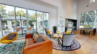 Located at 890 Church St in Mountain View, California, this single-story community clubhouse is a thoughtfully designed gathering space that blends modern aesthetics with warm, inviting details. The interior is anchored by soaring vaulted ceilings that create an airy, expansive atmosphere, complemented by crisp white walls and rich herringbone-patterned hardwood flooring throughout.

The main lounge area is furnished with a bold cognac leather sofa, eclectic accent chairs in vibrant yellows and oranges, and layered patterned area rugs, all contributing to a lively yet comfortable atmosphere. Large floor-to-ceiling sliding glass doors line one wall, flooding the space with abundant natural light and providing a seamless visual and physical connection to an outdoor patio equipped with seating, umbrella tables, and a barbecue grill.

A tucked-away reading nook features built-in upholstered bench seating in soft grey velvet, flanked by elegant brass wall sconces and framed by a dramatic tall window overlooking mature trees and the surrounding neighborhood streetscape.

Toward the back of the space, a sleek built-in kitchenette finished in dark cabinetry offers counter space and appliances, ideal for casual gatherings. The entry corridor is lined with white-framed windows that draw in additional natural light and offer views of manicured landscaping just outside. Together, these elements create a polished, community-centered space that is both functional and visually engaging.