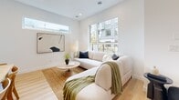 Located in Surrey, BC, this contemporary multi-floor home offers three bedrooms, three bathrooms, and a thoughtfully designed layout spread across three levels. The main floor hosts an open-concept kitchen and living room bathed in natural light from large windows overlooking the surrounding neighbourhood. The kitchen is a standout feature, showcasing two-tone cabinetry — warm wood lower drawers paired with light grey upper cabinets — complemented by a stainless steel appliance package, a French-door refrigerator, gas range, and a sleek white quartz island with bar seating and light wood accents. Light hardwood flooring runs throughout the main level, adding warmth to the crisp white palette. The living room is bright and inviting, with floor-to-ceiling windows and access to an outdoor balcony area. Each bathroom continues the modern aesthetic with warm wood vanities, matte black hardware, light tile flooring, and clean white walls. The primary bedroom is a comfortable retreat, featuring plush carpet, a large sliding glass door for natural light, and a serene, neutral ambiance. Additional bedrooms are carpeted and well-proportioned, with clerestory-style windows providing light and privacy. Staircases connect all three floors efficiently, with hallways and a closet adding practical storage and circulation throughout this well-appointed home.