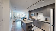 This well-appointed one-bedroom, one-bathroom residence offers a thoughtfully designed open-concept layout that maximizes both functionality and style. The combined kitchen and living area serves as the heart of the home, featuring a sleek, modern kitchen outfitted with dark gray flat-front cabinetry, white subway tile backsplash, granite countertops, and a full suite of stainless steel appliances including a gas range, built-in microwave, dishwasher, and refrigerator. A freestanding kitchen island with a granite top and bar seating provides additional prep space and casual dining. Track lighting overhead adds a contemporary touch throughout. Light hardwood-style flooring flows seamlessly into the living area, which is brightened by large windows that invite natural light and outdoor views. The bedroom is a serene retreat with windows on two sides, offering ample natural light. It is served by a generously sized walk-in closet outfitted with full wire shelving systems along multiple walls, providing extensive storage. The bathroom features large-format tile flooring, a white vanity with granite countertop, and a well-lit mirror. A dedicated hallway connects all rooms, completing this efficiently designed, modern residence.