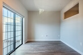 Located at 105 Water St in Waunakee, WI, this well-designed one-bedroom, one-bathroom unit offers a smart and functional layout across a single floor. The entrance leads into an open living and kitchen area finished with light-toned hardwood-style flooring and recessed lighting throughout. The kitchen is a standout feature, equipped with rich dark-stained cabinetry, light quartz countertops, a subway tile backsplash, stainless steel appliances including an electric range, over-the-range microwave, dishwasher, and refrigerator, along with a deep undermount sink. A large grid-pane window at the end of the kitchen area fills the space with natural light. A stylish sliding barn door adds a modern architectural touch to the interior hallway. The bedroom is a cozy, carpeted retreat featuring a ceiling fan, a high transom-style window for natural light, and direct access to a dedicated closet as well as a separate laundry area. The bathroom offers a dark-stained vanity with a white countertop, a full tub-shower combination with tiled surround, and wood-look vinyl flooring. Clean neutral wall tones and consistent finishes throughout create a cohesive, modern aesthetic.