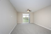 This single-floor space is designed with a cohesive, neutral color palette and modern finishes that create a clean, functional environment. The open-concept living area is generously proportioned, featuring soft wall-to-wall carpeting in a light gray tone and warm beige walls. A ceiling fan with a light fixture anchors the room, providing both airflow and ambient lighting. The space flows seamlessly toward a peninsula-style kitchen, which is illuminated by pendant lighting overhead.

The kitchen is outfitted with dark espresso-toned cabinetry featuring sleek hardware, light granite-style countertops, and stainless steel appliances including a gas range, over-the-range microwave, and a full-size refrigerator. Stone-look tile flooring adds durability and visual contrast to the darker cabinetry.

The bedroom mirrors the living area with plush carpeting, a ceiling fan, and neutral beige walls, providing a comfortable and versatile space. The bathroom continues the design language of the rest of the unit, featuring matching dark cabinetry, a granite-style countertop with an integrated sink, a large vanity mirror, and the same stone-look tile flooring, resulting in a polished and consistent finish throughout.