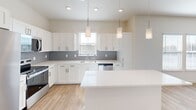 Located at 9000 Little Palm Way in Venice, FL, this thoughtfully designed two-story home offers a bright, modern interior spread across two floors. The ground floor is anchored by an open-concept kitchen and combined dining and living area, ideal for everyday living and entertaining. The kitchen is a standout feature, showcasing crisp white shaker cabinetry, a grey subway tile backsplash, gleaming quartz countertops, a central island, and stainless steel appliances including a range, microwave, dishwasher, and refrigerator. Three pendant lights hang above the space, complementing the vaulted ceiling and multiple windows that flood the area with natural light. Light wood-style flooring runs throughout, adding warmth to the clean, neutral palette. The entrance provides a welcoming transition into the home, with staircase access leading to the upper floor. Upstairs, the generously sized primary bedroom features dual windows and a ceiling fan, while two closets offer ample storage. The full bathroom includes a large vanity with quartz countertop and a wide mirror. A dedicated laundry room houses a full-size washer and dryer. Outside, a private fenced yard with lush turf and a white vinyl privacy fence creates a serene outdoor retreat, accented by Florida-style landscaping.
