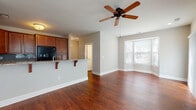 This two-floor home offers a well-designed layout with a blend of functional and comfortable living spaces throughout. The main level opens into a bright living area highlighted by rich hardwood flooring, a ceiling fan, and a charming bay window that invites abundant natural light. The kitchen is appointed with warm cherry wood cabinetry, granite countertops, a tiled backsplash in a soft blue-gray hue, and black appliances including a gas range, built-in microwave, and refrigerator. A breakfast bar peninsula connects the kitchen seamlessly to the living area. A dedicated laundry room with a full-size washer and dryer adds everyday convenience, and an attached garage with interior access provides additional storage and parking. The upper level features a generously sized primary bedroom with soaring vaulted ceilings, a ceiling fan, and multiple windows that fill the space with natural light. This suite includes a spacious walk-in closet with wire shelving and an en-suite bathroom complete with a granite vanity and a glass-enclosed walk-in shower. An additional bedroom with plush carpeting, a double-door closet, and a window overlooking greenery, along with a second full bathroom featuring tile flooring and a granite vanity, round out the upper level.