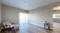 This single-story space in Brentwood, California (94513) presents a clean, neutral aesthetic throughout its well-connected floor plan. Wood-style flooring runs consistently across all areas, complementing the soft gray and beige wall tones that create a calm, cohesive atmosphere.

The main living area is notably open and bright, featuring a large sliding glass door dressed with vertical blinds that allow abundant natural light to filter in. A ceiling fan is installed overhead, adding both functionality and a finishing detail to the space. The open layout, as visible in the 3D floor plan, connects the living area to the kitchen and additional rooms in a logical flow.

The galley-style kitchen is efficiently arranged, featuring white cabinetry, dark countertops, a double sink, and a window that brings in natural light. Appliances include a refrigerator and range.

Additional rooms feature windows with horizontal blinds, providing natural light and views of the surrounding neighborhood. The bathroom is appointed with wood-style flooring consistent with the rest of the space, and includes a toilet and towel bars. White baseboards frame each room, adding a clean, finished look throughout the entire space.