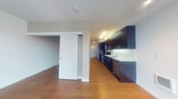 Located on the third floor at 407 NE Mason St in Portland's vibrant NE neighborhood, this contemporary apartment offers a well-designed, single-level layout with clean finishes throughout. Warm hardwood flooring runs seamlessly across the open-plan living and kitchen areas, creating a cohesive and inviting atmosphere. The galley-style kitchen is outfitted with dark espresso cabinetry extending to the ceiling for ample storage, white quartz countertops, a classic white subway tile backsplash, and a full suite of stainless steel appliances including a refrigerator, electric range, microwave, and dishwasher. A sliding door separates the living area from an adjacent room, offering flexible use of the space. Large windows fitted with horizontal blinds flood the living area and bedroom with natural light and provide views of the surrounding neighborhood's treetops. The bedroom features a dedicated walk-in closet for generous storage. The bathroom is finished with a dark-cabinetry vanity, white quartz countertop, and a large mirror, while a stacked washer and dryer unit is conveniently accessible nearby. The overall aesthetic is modern and minimalist, with crisp white walls, recessed and track lighting, and thoughtful built-in storage throughout.