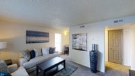 Located at 10701 North Pecos Street in Northglenn, Colorado, this single-floor residential unit offers a practical and comfortable layout designed for everyday living. The living area serves as the heart of the space, featuring wall-to-wall carpet flooring that adds warmth underfoot. Neutral-toned walls provide a versatile backdrop, easily complemented by a variety of décor styles, as demonstrated by the bold canvas artwork adorning the walls. A textured ceiling adds subtle visual interest throughout. Natural light filters in through a window, brightening the living area and creating an inviting atmosphere. The open sightline from the living room into an adjoining area — visible in the background — suggests a connected, functional floor plan that facilitates easy movement between spaces. Decorative accents, such as a tall statement vase, highlight the potential for personalization within the unit. The overall ambiance is calm and neutral, making it well-suited for those seeking a straightforward, move-in-ready residence in the Northglenn community, with convenient access to the amenities and services the surrounding area has to offer.