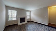 This single-story, 1-bedroom, 1-bathroom unit in Memphis, Tennessee offers a well-organized layout with a clean, move-in-ready aesthetic throughout. The living room serves as the focal point of the home, anchored by a white brick fireplace and framed by multiple windows fitted with blinds that invite natural light while maintaining privacy. Dark hardwood-style flooring runs throughout the main living areas, adding warmth and a modern touch. Adjacent to the living room, a dedicated dining area features a pendant light overhead and connects seamlessly to the kitchen via a pass-through countertop, creating an open, convenient flow. The kitchen is equipped with rich cherry-toned cabinetry, granite-style countertops, and black appliances including a refrigerator, electric range, and over-the-range microwave, along with wood-look flooring that ties the space together. The bedroom offers a comfortable, carpeted retreat with a ceiling fan and ample wall space. The bathroom includes a tiled tub-shower combination, matching cabinetry, and wood-look flooring. Neutral wall tones and clean finishes throughout give this unit a cohesive and inviting character well-suited for everyday living in Memphis.