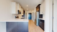 This contemporary single-floor unit offers a thoughtfully designed layout with modern finishes throughout. The kitchen is a standout feature, showcasing a two-tone cabinetry scheme that pairs crisp white upper cabinets with rich dark lower cabinets, all complemented by clean white quartz countertops and a classic subway tile backsplash. Stainless steel appliances, including a refrigerator, range, and over-the-range microwave, complete the space. Light hardwood-style flooring runs throughout the main living and kitchen areas, lending warmth and continuity to the open layout.

The bedrooms are finished with neutral carpet and benefit from large black-framed windows that bring in generous natural light and offer elevated views of the surrounding neighborhood. One room also features access to a private balcony through full-height sliding glass doors, extending the living space outdoors and framing a bright, open skyline view.

The bathroom is well-appointed with dark espresso cabinetry, white quartz countertops, a large vanity mirror, and a walk-in tiled shower enclosed by sliding glass doors. Light wood-style flooring ties the bathroom together with the rest of the unit. Overall, the space presents a clean, modern aesthetic with a cohesive palette of light neutrals and dark contrasting accents.