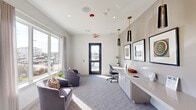 Located at 12202 Huffmeister Road in Cypress, Texas, this well-appointed single-level room serves as a versatile communal or office space within a larger residential community. The interior is finished in a clean, contemporary style, with neutral white walls, recessed lighting, and patterned carpet flooring that adds subtle texture underfoot.

Large windows along one wall flood the space with abundant natural light, framing views of the outdoor pool area and surrounding residential buildings—creating a bright, welcoming atmosphere throughout the day. Elegant drapes frame the windows, adding a soft, polished touch to the overall design.

A built-in white countertop workstation runs along one wall, paired with white cabinetry below and a task chair, providing a functional workspace. Overhead, sleek black-and-gold pendant lights add a stylish accent. Framed artwork displayed along the wall contributes a curated, refined aesthetic.

A seating area with upholstered armchairs and colorful accent pillows offers a comfortable lounge setting. A glass-paneled exterior door provides direct outdoor access and additional light. A connecting doorway leads to adjacent spaces, suggesting the room functions as part of a broader amenity suite.