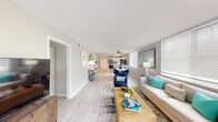 This single-floor residence offers a thoughtfully designed layout with a cohesive coastal aesthetic woven throughout. Light wood-tone flooring runs continuously across the main living areas, complementing soft neutral wall tones and aqua and navy accent decor.

The living room is generously proportioned, bathed in natural light from large windows fitted with horizontal blinds. A sliding glass door opens to a private balcony with views of lush greenery, extending the sense of space outdoors. The open layout flows seamlessly into a dedicated dining area, which benefits from abundant window light and ceiling fan ventilation.

The kitchen is well-appointed with white shaker cabinetry, a grey subway tile backsplash, light quartz countertops, and a full suite of stainless steel appliances including a refrigerator, range, microwave, and dishwasher. A hallway connecting the main living spaces features decorative wall art, reinforcing the home's coastal character.

The bedrooms offer comfortable retreats, each styled with calming blue-green tones. The bathroom includes a tiled shower-tub combination, toilet, and vanity with clean, neutral finishes. Throughout the residence, natural light, consistent flooring, and a serene color palette create a bright and welcoming atmosphere.