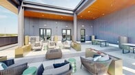 Located at 1827 N Meridian St in Indianapolis, Indiana, this rooftop amenity level offers a sophisticated outdoor retreat designed for relaxation and social gathering. The space is defined by its expansive open-air terrace, finished with large-format porcelain tile flooring that extends throughout the entire level, creating a clean and cohesive aesthetic.

A partially covered pergola structure with a warm wood-paneled ceiling and integrated recessed lighting provides a comfortable shaded gathering area, furnished with an eclectic mix of woven rope lounge chairs, accent stools, and fire pit tables. The open sections of the terrace extend outward, offering unobstructed panoramic views of the Indianapolis skyline and surrounding Meridian-Kessler neighborhood, best appreciated from the bar-height balcony seating area along the perimeter railing.

Additional dining and casual seating zones are arranged throughout, featuring slatted wood tables paired with powder-coated metal chairs, ideal for both intimate conversations and larger group gatherings. Architectural panel walls in a muted gray tone frame the space and provide privacy while contributing to the modern, urban design language.

Glass-paned doors connect the outdoor terrace to interior amenity spaces, and prominent signage ensures clear circulation. The overall ambiance is contemporary and inviting, blending industrial structural elements with warm finishes and vibrant outdoor furnishings to create a dynamic rooftop experience above the heart of Indianapolis.