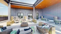 Located at 1827 N Meridian St in Indianapolis, Indiana, this rooftop amenity level offers a sophisticated outdoor retreat designed for relaxation and social gathering. The space is defined by its expansive open-air terrace, finished with large-format porcelain tile flooring that extends throughout the entire level, creating a clean and cohesive aesthetic.

A partially covered pergola structure with a warm wood-paneled ceiling and integrated recessed lighting provides a comfortable shaded gathering area, furnished with an eclectic mix of woven rope lounge chairs, accent stools, and fire pit tables. The open sections of the terrace extend outward, offering unobstructed panoramic views of the Indianapolis skyline and surrounding Meridian-Kessler neighborhood, best appreciated from the bar-height balcony seating area along the perimeter railing.

Additional dining and casual seating zones are arranged throughout, featuring slatted wood tables paired with powder-coated metal chairs, ideal for both intimate conversations and larger group gatherings. Architectural panel walls in a muted gray tone frame the space and provide privacy while contributing to the modern, urban design language.

Glass-paned doors connect the outdoor terrace to interior amenity spaces, and prominent signage ensures clear circulation. The overall ambiance is contemporary and inviting, blending industrial structural elements with warm finishes and vibrant outdoor furnishings to create a dynamic rooftop experience above the heart of Indianapolis.