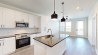 Located at 201 Hills Rd in Panama City Beach, Florida, this thoughtfully designed one-bedroom, one-bathroom residence offers a clean, modern aesthetic throughout its efficiently utilized single floor. The open-concept kitchen and living area serves as the heart of the home, showcasing white shaker-style cabinetry that extends to the ceiling, dark countertops, a subway tile backsplash, and a full suite of stainless steel appliances including a French door refrigerator, electric range, and built-in microwave. A central island with pendant lighting provides additional workspace and casual dining potential, while light-toned hardwood-style flooring flows seamlessly throughout the entire space. The living area is bathed in natural light through large windows and features direct access to a private balcony, offering outdoor views of the surrounding landscape. Crown molding and ceiling fans add refined detail to the living and bedroom spaces. The generously sized bedroom includes dual windows with outdoor views and connects to a spacious walk-in closet outfitted with multi-tier wire shelving. The bathroom is well-appointed with white vanity cabinetry, dark countertops, and a sleek frameless sliding glass shower enclosure, maintaining the home's consistent modern design language.