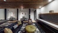 Located at 701 Easley Bridge Road in Greenville, SC, this single-floor amenity space is a thoughtfully designed lounge and entertainment area that blends industrial character with modern comfort. The space is anchored by bold, dark structural columns that rise from polished concrete floors, adding an unmistakably industrial edge to the interior. A rich wood-paneled ceiling runs overhead, providing warmth and contrast against the crisp white walls.

The game and entertainment area takes center stage, featuring a full-size billiards table set atop a graphic, abstract area rug. Cue racks are mounted along the walls, and pendant lighting drops from the ceiling to illuminate the table below. A wall-mounted flat-screen television is positioned prominently, making the space equally suited for watching and playing.

Adjacent to the game area is a comfortable lounge zone furnished with a sleek black sofa, a tufted olive-green leather ottoman, and a leather accent chair with ottoman, all arranged for relaxed conversation or media viewing. A built-in media console with cabinetry provides additional functionality along one wall.

Throughout the space, vibrant pop art prints — depicting stylized spray cans labeled with expressive titles — are displayed in coordinated pairs above intimate bistro tables with white counter-height stools. These artistic vignettes add energy and personality, making this lounge a visually dynamic and inviting gathering space.