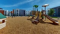 Located at 1161 E O'Neil Dr in Casa Grande, Arizona, this outdoor playground area serves as a central recreational amenity within a contemporary multi-building residential community. The space is designed to provide a safe and engaging environment for children of various ages, set against the backdrop of the community's modern architecture, which features bold exterior color contrasts including terracotta orange, charcoal gray, and crisp white facades with private balconies.

The playground is surfaced throughout with a generous layer of wood chip mulch, providing impact-absorbing coverage across the entire area. A multi-level play structure forms the centerpiece, offering an assortment of activities including spiral and straight slides, climbing nets, staircases, and overhead canopy elements in green and tan tones. A dedicated swing set, featuring a covered pergola-style frame and multiple bench swings, occupies one section of the space.

The surrounding landscape incorporates desert-adapted plantings, decorative rock, and young trees that contribute to a low-maintenance, Arizona-appropriate aesthetic. The open layout ensures clear sightlines across the play area. Under Casa Grande's abundant sunshine and open blue skies, the playground offers a bright, welcoming outdoor gathering space for the community.