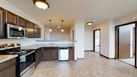This single-floor unit offers a practical and well-organized layout across several interconnected rooms. The kitchen is a standout feature, outfitted with rich, dark cabinetry, stainless steel appliances including a refrigerator, range, microwave, and dishwasher, and light-toned countertops. The flooring throughout the kitchen and adjoining areas features a warm stone-look tile, adding a durable and cohesive aesthetic. Pendant lighting hangs above the kitchen peninsula, providing task lighting and a subtle design element that complements the overall scheme.

The bedrooms are carpeted in neutral tones and receive natural light through large windows that frame urban cityscape views. One bedroom includes a ceiling fan, while another is equipped with a wall-mounted split-system air conditioning unit, offering individual climate control. Both rooms provide a calm, functional environment.

The bathroom is finished with the same tile flooring found in the kitchen and features a full tub-shower combination, toilet, and dark wood vanity, maintaining a consistent design language throughout the unit.

A walk-in closet or storage room is accessible from one of the bedrooms, adding practical storage capacity. The overall ambiance is clean and neutral, making the space move-in ready and adaptable to a variety of furnishing styles.