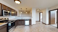 This single-floor unit offers a practical and well-organized layout across several interconnected rooms. The kitchen is a standout feature, outfitted with rich, dark cabinetry, stainless steel appliances including a refrigerator, range, microwave, and dishwasher, and light-toned countertops. The flooring throughout the kitchen and adjoining areas features a warm stone-look tile, adding a durable and cohesive aesthetic. Pendant lighting hangs above the kitchen peninsula, providing task lighting and a subtle design element that complements the overall scheme.

The bedrooms are carpeted in neutral tones and receive natural light through large windows that frame urban cityscape views. One bedroom includes a ceiling fan, while another is equipped with a wall-mounted split-system air conditioning unit, offering individual climate control. Both rooms provide a calm, functional environment.

The bathroom is finished with the same tile flooring found in the kitchen and features a full tub-shower combination, toilet, and dark wood vanity, maintaining a consistent design language throughout the unit.

A walk-in closet or storage room is accessible from one of the bedrooms, adding practical storage capacity. The overall ambiance is clean and neutral, making the space move-in ready and adaptable to a variety of furnishing styles.