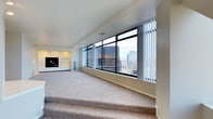 Located at 3701, this single-floor high-rise space offers an impressive urban living experience defined by its commanding city skyline views and thoughtfully designed interior. The main living area is a standout feature, showcasing an expansive wall of floor-to-ceiling windows fitted with vertical blinds, flooding the space with abundant natural light while framing dramatic panoramic views of the surrounding cityscape and mountain backdrop beyond. Plush, neutral-toned carpeting covers the raised living area, lending warmth and comfort underfoot. A subtle split-level design adds architectural interest, with a step-up platform area that further emphasizes the sweeping views. The walls are finished in clean, crisp white tones that enhance the sense of brightness and openness throughout. A built-in entertainment niche anchors one wall, providing a sleek, integrated focal point for the living space. Recessed ceiling details and visible HVAC vents reflect practical, modern construction. The overall ambiance is clean, airy, and contemporary, with the ever-present city views creating a dynamic and inspiring backdrop that shifts with the light throughout the day.