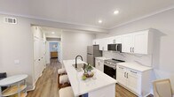 This 880-square-foot, single-story residence in Covington features 2 bedrooms, 2 bathrooms, and a combined kitchen and living area, all finished with warm hardwood-style flooring and neutral gray walls that create a cohesive, modern aesthetic throughout.

The open-concept kitchen is a standout feature, showcasing white shaker cabinets with matte black hardware, a striking quartz countertop with marble-like veining, a navy blue shiplap island with bar seating for three, stainless steel appliances, and a matte black sink faucet. Adjacent to the kitchen, the living room offers recessed lighting, crown molding, and a windowed exterior door that invites natural light.

The primary bedroom spans 160 square feet and features multiple windows with decorative curtains, providing ample natural light. A dedicated closet adds practical storage. The second bedroom is equally well-lit and includes its own closet space. Both rooms carry a calm, restful atmosphere with soft neutral tones.

The two bathrooms are finished in crisp white with matte black fixtures and hardware. One bathroom features a large arched gold-framed mirror and a full-length vanity with an undermount sink, while the other offers a clean, minimal design with framed wall art and wood-look flooring. The unit also includes one additional closet for storage.