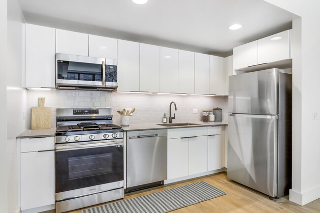 Renovated Package I kitchen with grey quartz countertops, white cabinetry, light grey tile backsplash, stainless steel appliances, and hard surface flooring - Avalon Morningside Park