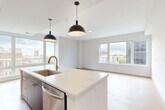 Located at 1557 Logan Street in Denver's Capitol Hill neighborhood, this well-appointed residence offers three bedrooms and three bathrooms across a thoughtfully designed single-floor layout. The open-concept kitchen and living area serves as the heart of the home, featuring a bold contrast of dark navy cabinetry and white quartz countertops, a large central island with a gold-accented sink, stainless steel appliances, and matte black pendant lighting. Expansive floor-to-ceiling windows flood the living area with natural light and frame sweeping views of the Denver skyline and surrounding urban landscape. Light wood-tone flooring runs consistently throughout the space, lending warmth and continuity. The primary bedroom is generously sized, complete with a walk-in closet equipped with built-in shelving and a spa-inspired en-suite bathroom featuring a dual-sink dark vanity, matte black fixtures, framed mirrors, and a glass-enclosed walk-in shower. Additional bedrooms include ample closet storage. Secondary bathrooms offer tub-shower combinations with tiled surrounds and coordinating matte black hardware. A sleek hallway with a sliding barn door connects the private quarters. The overall aesthetic is clean, modern, and cohesive throughout.