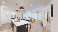 This well-designed 2-bedroom, 2-bathroom single-floor residence offers a clean, contemporary aesthetic with an open-concept layout that seamlessly connects the kitchen, dining, and living areas. The kitchen is a standout feature, outfitted with dark cabinetry, white quartz countertops, stainless steel appliances, a herringbone tile backsplash, and a central island with bar seating illuminated by stylish pendant lights. Light wood-look flooring flows throughout the main living areas, enhancing the bright, airy feel. The living room receives generous natural light through large windows and a glass door, while recessed lighting adds warmth throughout. A dedicated dining area accommodates a round table and connects easily to the adjacent rooms. The spacious primary bedroom features plush carpet, recessed lighting, and access to a walk-in closet with dual hanging rods and shelving. The second bedroom is well-lit with multiple windows and sheer curtains. Both bathrooms are finished with dark vanities and light wood-tone flooring. A dedicated closet provides additional storage. The overall design is cohesive and modern, emphasizing neutral tones, functional layouts, and quality finishes throughout.