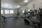 This fitness center is designed to provide a functional and motivating workout environment. The space features dramatically vaulted ceilings that create an open, airy atmosphere, enhanced by strategically placed ceiling fans that promote air circulation throughout. High clerestory windows along the upper walls allow natural light to filter in, contributing to the bright and energetic ambiance.

Full-length wall mirrors line a significant portion of the space, visually expanding the room and allowing users to monitor their form during exercise. The flooring consists of durable rubber matting, providing both safety and comfort underfoot. Motivational typography and fitness-themed artwork are displayed prominently on the walls, reinforcing an encouraging atmosphere.

The cardio section is well-stocked with treadmills, elliptical trainers, stationary bikes, and a rowing machine, the majority from the SportsArt brand. A wall-mounted flat-screen television is positioned for easy viewing during workouts. The strength-training area includes a multi-station cable machine, an adjustable weight bench, and a tiered dumbbell rack offering a range of free weights. A water station and additional utility areas are accessible through a doorway at the rear of the space, adding convenience to the overall facility.