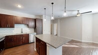 Located at 3700 Windhaven Pkwy in Lewisville, TX, this thoughtfully designed one-bedroom, one-bathroom residence offers a comfortable and functional layout across a single floor. The open-concept kitchen and living area serves as the heart of the home, showcasing rich dark wood cabinetry, granite countertops, a classic subway tile backsplash, and a full suite of stainless steel appliances including a refrigerator, range, microwave, and dishwasher. A central kitchen island with pendant lighting provides additional prep space and a natural gathering point. Warm wood-style flooring flows consistently throughout the unit, lending a cohesive and polished aesthetic. The bedroom is generously proportioned, featuring a ceiling fan, natural light from large windows, and access to an outdoor area via a glass door. The room connects to a well-sized closet, providing ample storage. The bathroom is finished with matching granite countertops, dark cabinetry, subway-tiled tub/shower surround, and wood-style flooring for a consistent design language. Additional conveniences include a dedicated laundry area with hookups, a pantry, and multiple closets for storage throughout the unit.