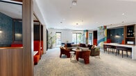 This contemporary coworking facility, located at 10 Tower St NW in Atlanta, offers 2,080 square feet of versatile workspace on a single floor. The space boasts a striking blend of modern design and functional elements, catering to various work preferences. Upon entry, visitors are greeted by a sleek reception area featuring a distinctive geometric floor pattern that continues throughout the space, unifying the design.

The open-plan layout incorporates a mix of seating options, from communal tables to comfortable lounge areas, fostering both collaboration and individual focus. Private booths with vibrant red upholstery provide quiet spaces for meetings or concentrated work. Floor-to-ceiling windows flood the area with natural light, while strategically placed pendant lights and LED strips ensure optimal illumination.

The interior showcases a sophisticated color palette of neutrals accented by bold reds and rich wood tones. Artistic elements, such as the unique wall installations and carefully curated artwork, add visual interest and inspire creativity. The space also features glass-walled meeting rooms and a kitchenette area, enhancing functionality for users.

High ceilings with exposed elements create an industrial-chic ambiance, while plush seating and abundant greenery soften the space, striking a balance between professional and comfortable. This thoughtfully designed coworking environment caters to modern professionals seeking a dynamic and inspiring workplace in Atlanta's bustling business district.