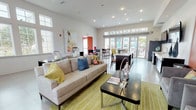 This single-floor community amenity space is thoughtfully designed to serve as a dynamic social hub, combining multiple functional zones within one open, flowing layout. The interior is defined by bold terracotta-red accent walls, warm wood-panel detailing, and light-toned tile flooring that runs throughout, creating a cohesive and energetic aesthetic.

The lounge area features a comfortable sectional sofa, accent chairs, and a coffee table arranged on a chartreuse area rug, anchored by wall-mounted flat-screen televisions. Adjacent to the lounge, a dedicated seating nook with navy blue booth-style chairs, a small table, and tall windows provides a quieter, more intimate setting ideal for individual work or conversation.

A generous full-length wet bar and kitchen counter runs along one side of the space, complete with dark cabinetry, white quartz countertops, a sink, under-counter refrigeration, and multiple wall-mounted screens — well-suited for social gatherings or catered events.

The dining and bar-height seating area accommodates multiple high-top tables with mixed colorful chairs, positioned to take full advantage of the expansive glass doors that open directly to an outdoor patio area. Transom windows above further enhance the sense of openness, flooding the interior with natural light and offering views of the surrounding outdoor amenities. Recessed lighting throughout ensures a bright, welcoming ambiance at any hour.