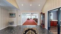 Located at 340 Providence Hill Drive in Ashland, Kentucky, this well-appointed single-story facility offers a generous and thoughtfully designed floor plan. The grand entrance foyer sets the tone with striking dark granite-look tile floors, vaulted ceilings, elegant striped wallcovering, and a stately grandfather clock, creating a welcoming first impression.

The expansive dining room is a standout feature, carpeted in rich red and lined with large floor-to-ceiling windows and sliding glass doors that frame sweeping panoramic views of the surrounding landscape. Vaulted ceilings and ceiling fans add to the airy, open ambiance, while multiple dining tables provide ample seating capacity.

The kitchen is fully equipped with rich cherry cabinetry, a cooktop range, refrigerator, and generous counter space. A brick-accented breakfast bar with rattan bar stools serves as both a functional and stylish transition between the kitchen and adjacent areas.

The living room features warm hardwood flooring, vaulted ceilings with a ceiling fan, tufted sofas, a stone-accented fireplace with a built-in media wall, and French doors leading to the office. Natural light pours in through multiple windows.

The private office space includes hardwood flooring, a conference table, and views of the surrounding greenery, accessible via elegant glass-paned French doors. Crown molding throughout the space adds a refined, polished finish.