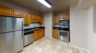 Located at 100 Kimball Ave in Salem, Virginia, this single-floor unit offers a practical and well-organized layout. The kitchen is a functional highlight, featuring warm honey-toned wooden cabinetry, dark countertops, and a full suite of stainless steel appliances including a refrigerator, electric range, over-the-range microwave, and dishwasher. Light-toned tile flooring and flush overhead lighting complete the space.

The living area is generously sized, finished with plush carpeting and neutral wall tones that create a calm, understated atmosphere. A sliding glass door opens to an outdoor balcony, allowing natural light to fill the room and providing outdoor views. The bedroom continues the same carpeted, neutral aesthetic and is equipped with a ceiling fan with integrated lighting, offering both comfort and air circulation. An additional carpeted room provides flexible space suitable for a second bedroom or office.

The bathroom is fitted with a full-size soaking tub and shower combination with tiled surround, alongside a standard toilet, all set within a clean, light-colored finish. Throughout the unit, consistent neutral paint tones, white trim, and carpeted flooring in the living and sleeping areas lend the space a cohesive, move-in-ready appearance.