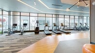 Located at 250 Martin Luther King Jr Dr SW in downtown Atlanta, this contemporary fitness center offers a sophisticated and well-equipped workout environment spread across a single, generously sized floor. The space is defined by its floor-to-ceiling glass curtain walls that flood the interior with natural light while framing striking panoramic views of the Atlanta skyline and surrounding landmarks.

The gym is organized into distinct functional zones, including dedicated areas for cardio equipment — featuring rows of treadmills, ellipticals, and stationary bikes — as well as strength training sections stocked with cable machines, free weights, kettlebells, and functional training rigs. A central open floor area with warm hardwood flooring serves as a versatile space for stretching, functional movement, or group training, complemented by patterned carpet tiles throughout the surrounding zones.

The interior design is modern and polished, with geometric hexagonal ceiling details, warm wood accents, and layered LED lighting that creates an energizing yet refined ambiance. A dedicated studio room with hardwood floors and a bold graphic accent wall offers space for focused training sessions. Motivational neon signage adds a dynamic, urban personality to the environment. The thoughtful layout and high-end finishes make this fitness center a standout amenity in the heart of Atlanta.