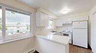 This single-floor residence offers a well-organized layout with three bedrooms, a kitchen, a pantry, and two closets. The kitchen is a standout feature, outfitted with crisp white cabinetry extending to the ceiling, a sleek white quartz peninsula countertop, hardwood-style flooring, and multiple windows that invite ample natural light. White appliances—including a refrigerator, electric range, and dishwasher—complete the clean, functional aesthetic. The kitchen transitions smoothly into the living area, which is finished with warm neutral carpet and features a sliding glass door that opens to a private balcony. From the balcony, residents enjoy a pleasant outdoor view of mature trees and a landscaped green space. The generously sized primary bedroom offers a comfortable retreat with soft carpet and ample room for furnishings. The additional bedrooms are well-proportioned, each with neutral carpet and sliding-door closets providing practical storage. A dedicated pantry adds to the overall storage capacity of the unit. Throughout the space, neutral walls, white trim, and consistent finishes create a cohesive, clean atmosphere. Baseboard heating is present in the living area, and a textured ceiling adds subtle visual character. The overall design is functional, light-filled, and move-in ready.