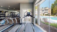 Located at 1301 Ivy Meadow Dr in Charlotte, NC, this single-floor fitness center is a comprehensively equipped facility designed to support a wide range of workout routines. The space is finished with durable rubber flooring throughout, neutral gray walls, and recessed lighting complemented by ceiling fans that maintain a comfortable environment during exercise.

The cardio zone features a row of TRUE-brand treadmills, elliptical trainers, a recumbent bike, and rowing machines, all positioned to take advantage of large windows and glass doors that flood the space with natural light and offer views of the outdoor pool and lush greenery. This connection to the outdoors creates an open, energizing atmosphere.

The strength training area is equally well-appointed, with a multi-station functional trainer, a punching bag, a full dumbbell rack with weights of varying sizes, a weight bench, and additional resistance machines. Floor-to-ceiling mirrors line the walls, visually expanding the space and allowing users to monitor their form during workouts.

Ceiling fans are distributed throughout to ensure consistent airflow, while recessed lighting provides bright, even illumination. The overall design is clean and modern, balancing practicality with a polished aesthetic that makes this fitness center a standout amenity for the Ivy Meadow community.